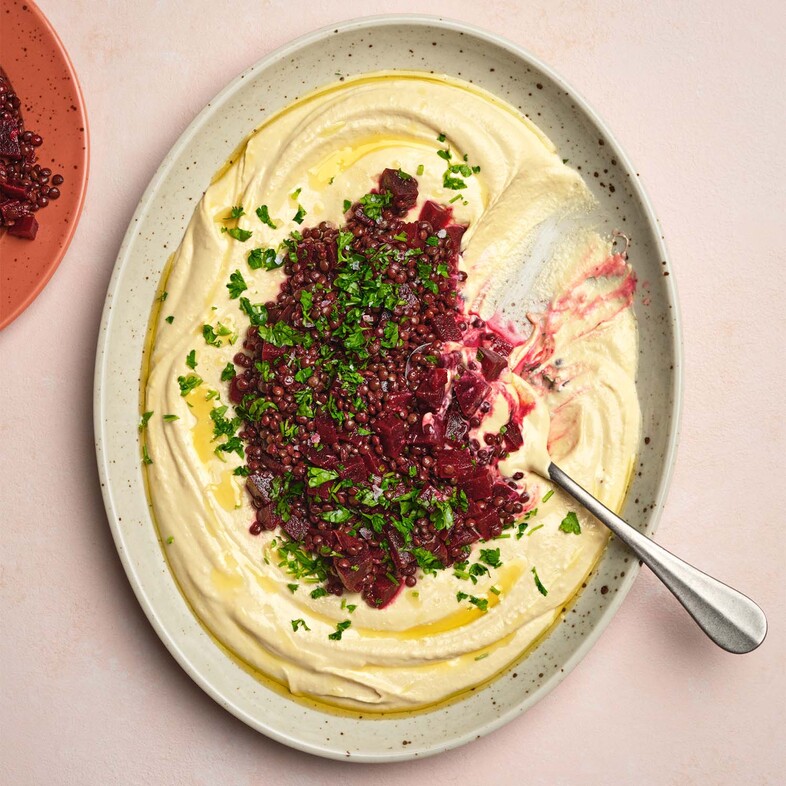 Krämig hummus med rödbetor och belugalinser i mitten, toppad med färsk persilja.