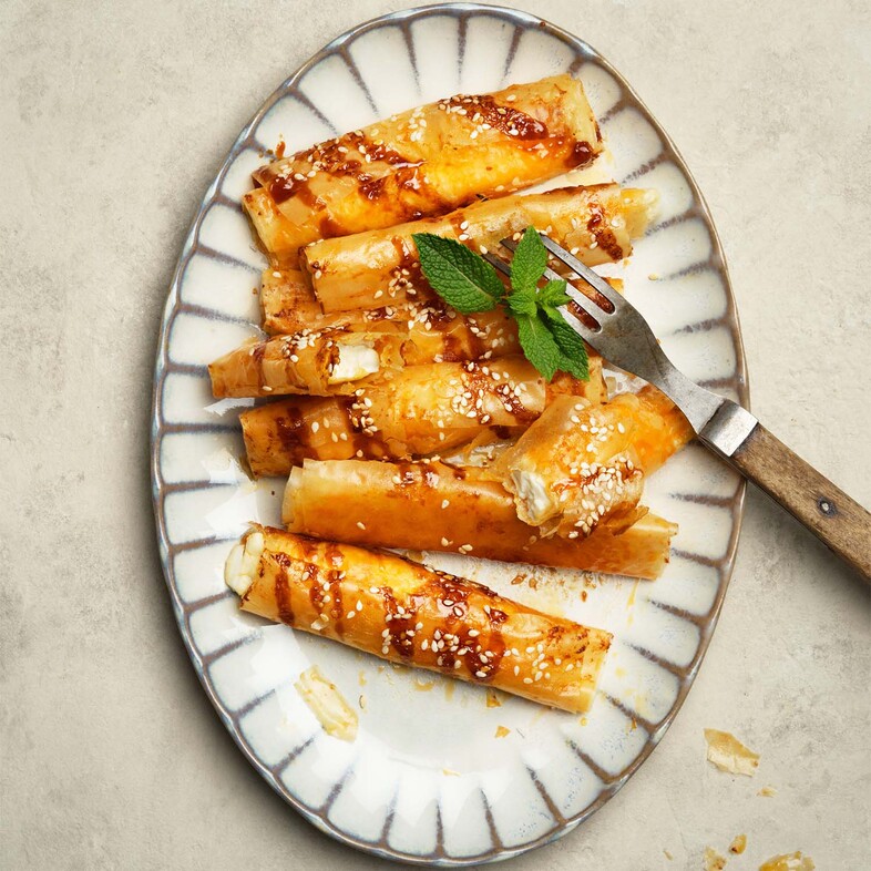 Krispiga filodegsrullar fyllda med fetaost och harissa, toppade med sesamfrön och ringlad dadelsirap.