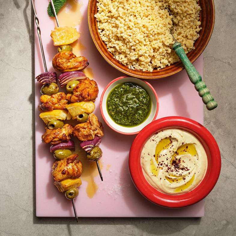 Grillade kycklingspett serverade med bulgur, hummus, zhug, rödlök och inlagd citron på ett fat