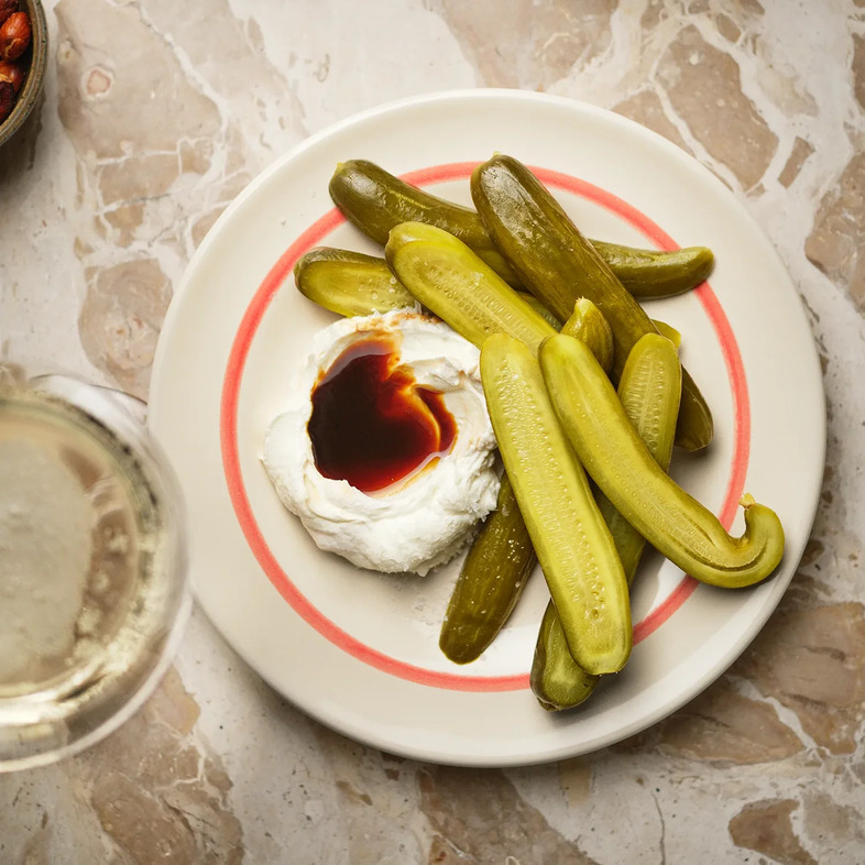 Krämig vit labneh upplagd på fat med en grop i mitten fylld med mörk dadelsirap, omgiven av gröna gurkor.