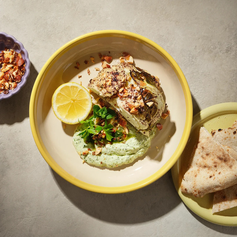 Ugnsrostade blomkålshalvor toppade med gröna örter, hackade mandlar och ringlad örtolja, serverade på en bädd av krämig ört- och yoghurtkräm.