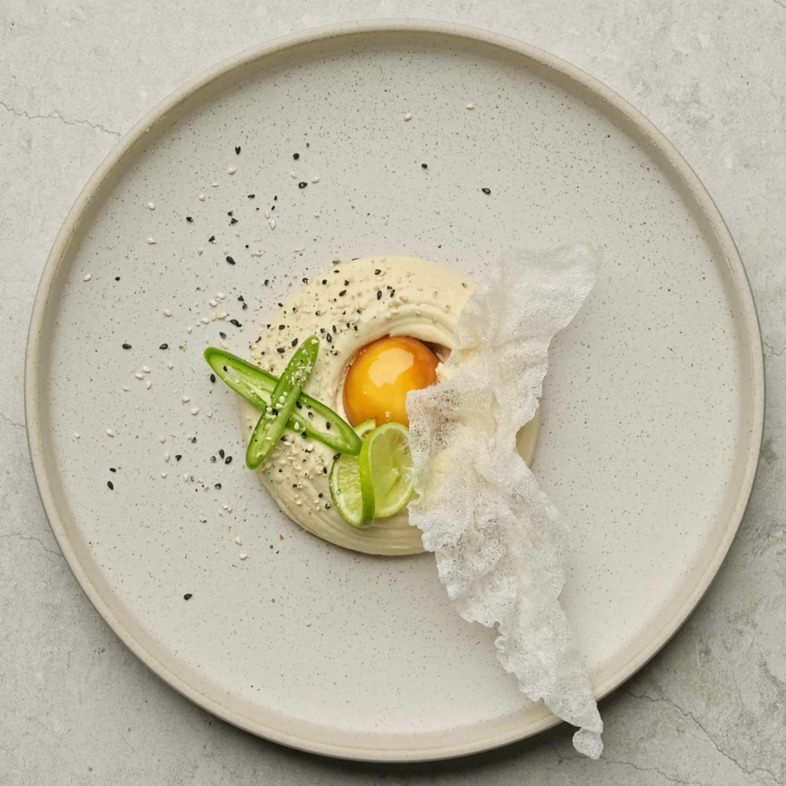 Hummus toppad med sojagravad äggula, friterat rispapper, rostade svarta och vita sesamfrön, lime och grön chili
